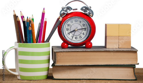 Alarm clock and books by colored pencils in mug on table