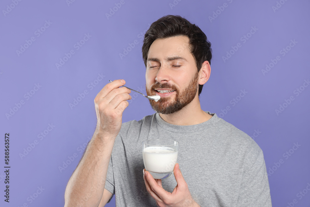 Handsome man eating delicious yogurt on violet background