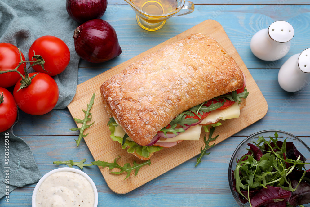 Delicious sandwich and fresh ingredients on light blue wooden table, flat lay