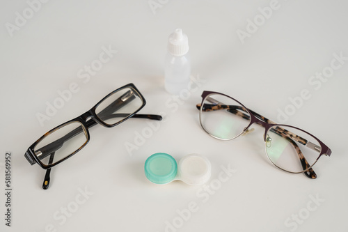 Two pairs of glasses lenses and contact drops in the eyes on a white table. 