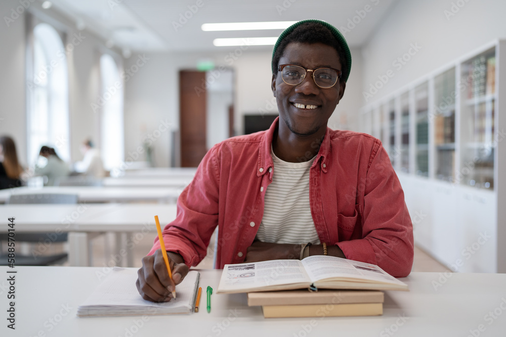 Positive African American man student studying in library making notes ...