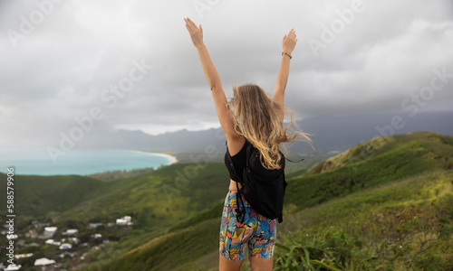 A woman hiker stands on the top of a mountain. Hawaiian nature overcast cloudy weather.