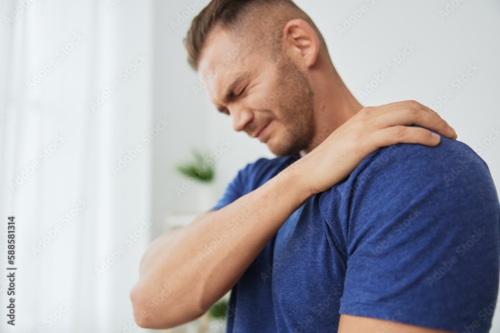 Man back neck and shoulder pain, inflammation of muscles and ligaments rupture during sports, inflammation and injury, in a blue t-shirt at home Man back neck and shoulder pain, inflammation of muscles and ligaments rupture during sports, inflammation and injury, in a blue t-shirt at home