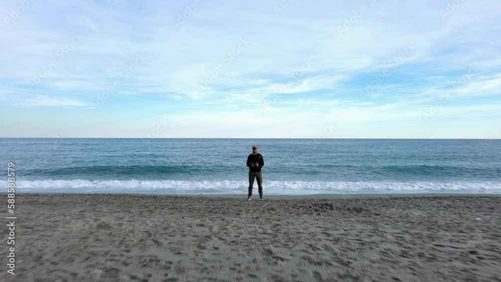 Drone pilot flies with drone overhead from beach to the open sea Drone pilot flies with drone overhead from beach to the open sea
