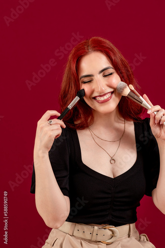Stylish woman holding make-up brushes while posing against an isolated background.
