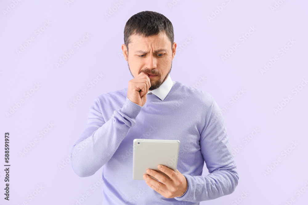 Handsome man with tablet computer biting nails on lilac background