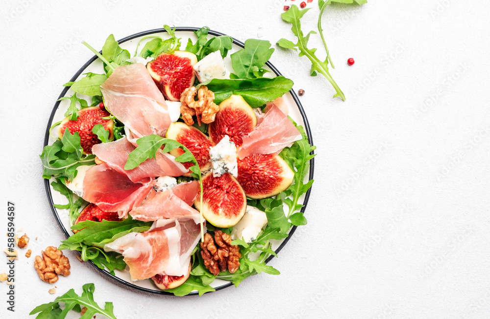 Summer salad with sweet figs, prosciutto, gorgonzola cheese, walnuts, arugula on white kitchen table background, top view, copy space