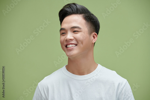 Portrait shot of young adult Asian man smiling posturing on green wall background