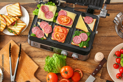 Modern electric grill with different delicious sandwiches on table