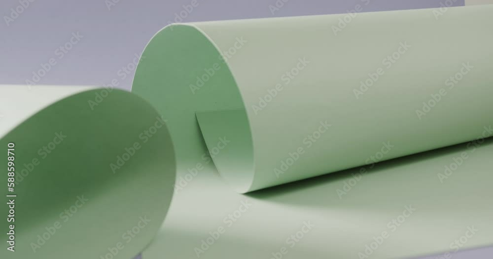 Close up of two pale green white rolled papers on blue background with copy space in slow motion Close up of two pale green white rolled papers on blue background with copy space in slow motion