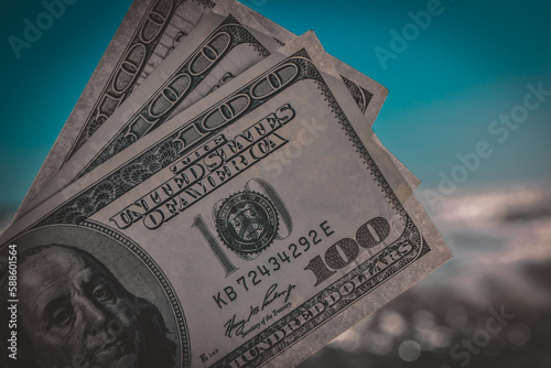 Girl holding money bill of 300 dollars on background of sea ocean waves and blue sky close-up. Hand wave sea ocean money dollars vacation. Concept finance money holiday traveling photo