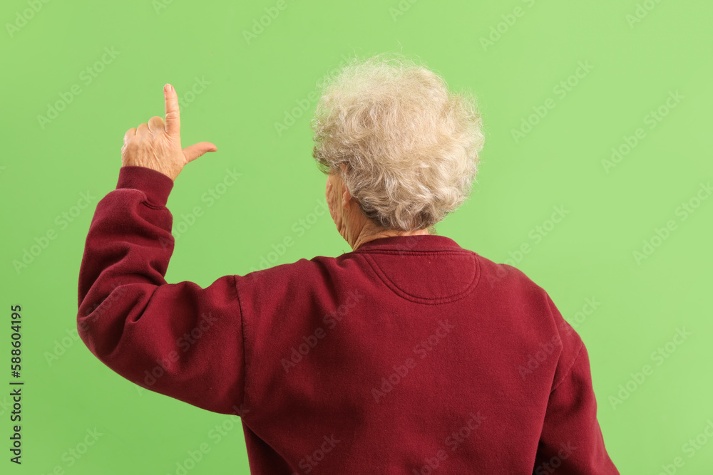 Senior woman showing loser gesture on green background, back view Senior woman showing loser gesture on green background, back view