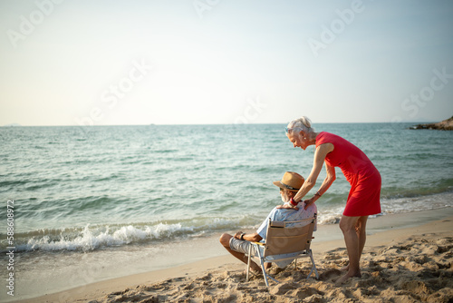 An elderly couple hugs their shoulders at the beach on their summer vacation and they smile and enjoy their vacation.