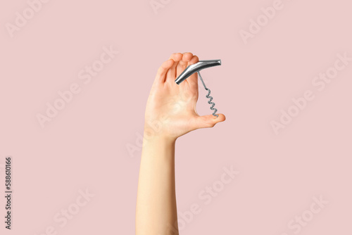 Female hand holding corkscrew on pink background