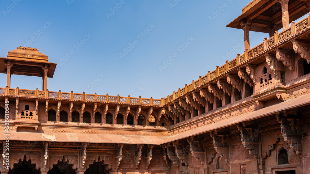 Details of the architecture of Jahangiri Mahal in the Red Fort. The upper part of the building with galleries, carved arches, a lattice fence along the roof, towers. Blue sky. India. Agra