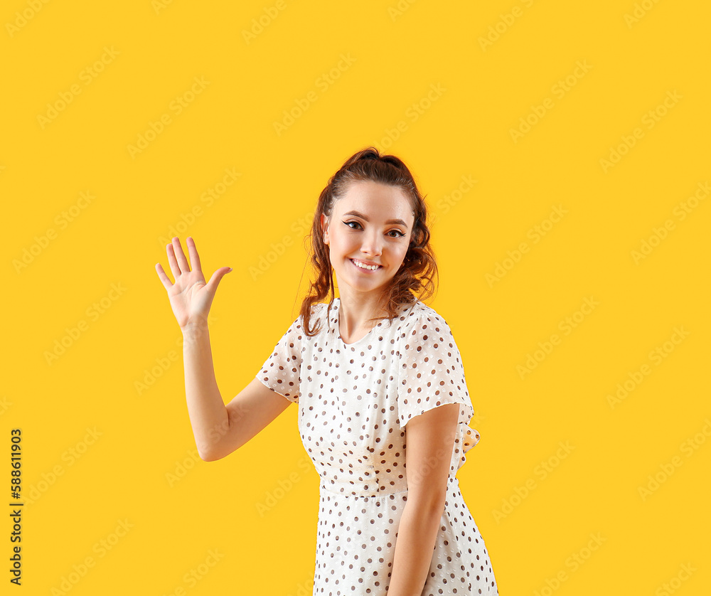 Beautiful young woman waving hand on yellow background Beautiful young woman waving hand on yellow background