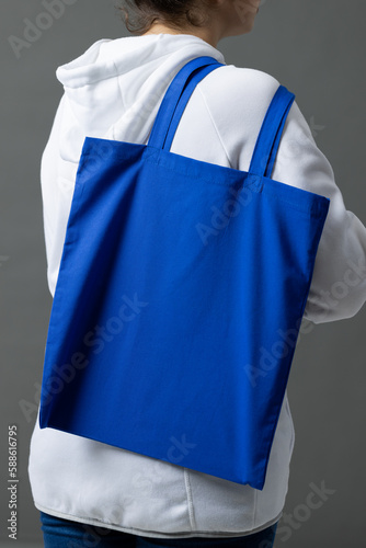 Caucasian woman holding over the shoulder blue canvas bag with copy space on grey background