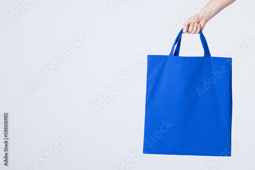 Hand of caucasian woman holding blue canvas bag with copy space on white background