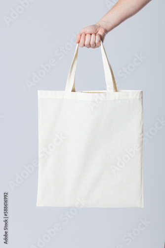Hand of caucasian woman holding white canvas bag with copy space on grey background