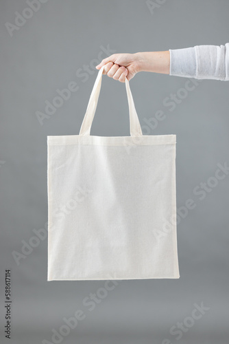 Hand of caucasian woman holding white canvas bag with copy space on grey background