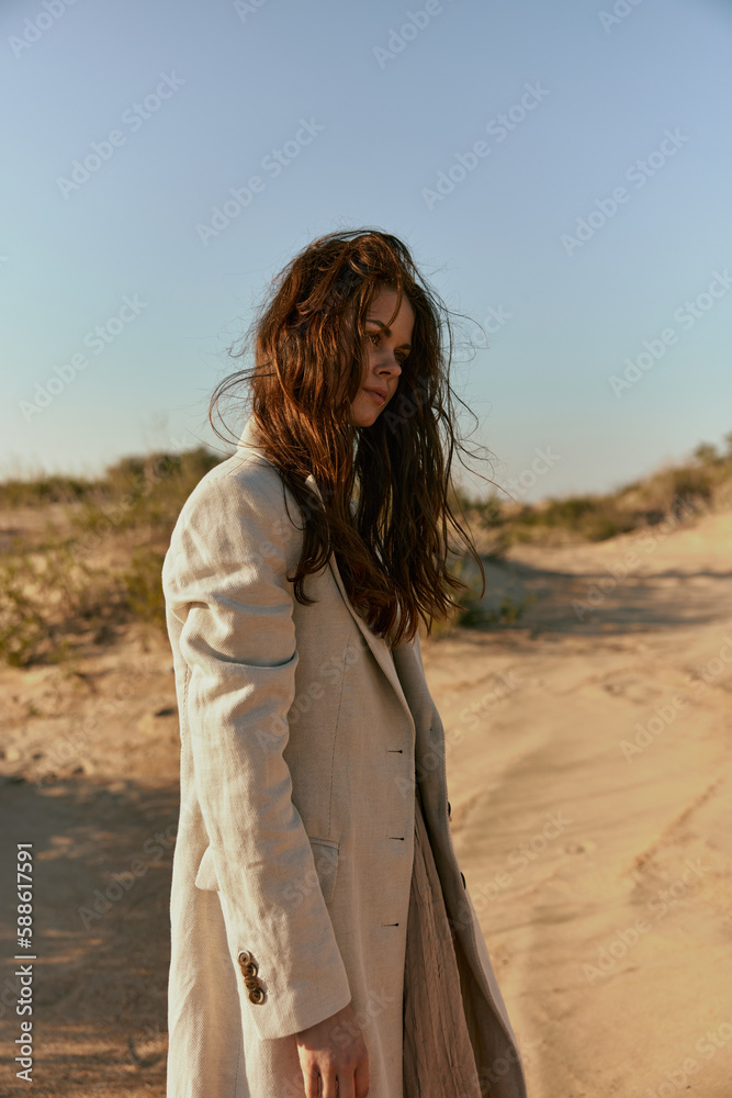 a stylish red-haired woman stands in the desert in light clothes in windy weather with her head down