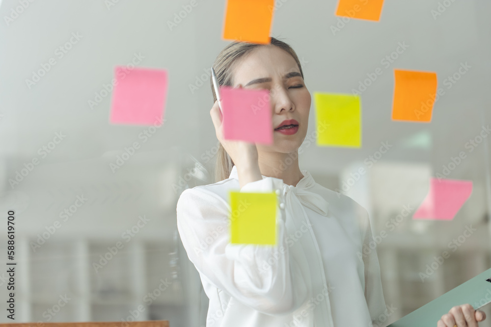 Asian woman working on project plan using sticky papers notes on glass wall, people meeting to share idea, Business design planning concepts. Asian woman working on project plan using sticky papers notes on glass wall, people meeting to share idea, Business design planning concepts.