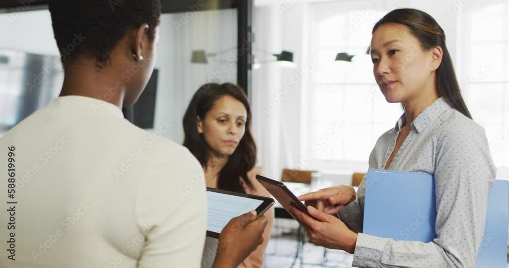 Diverse businesswomen using tablets and talking in casual office meeting Diverse businesswomen using tablets and talking in casual office meeting