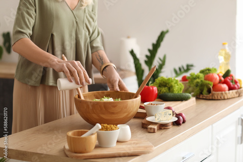 Mature woman making vegetable salad at table in kitchen, closeup