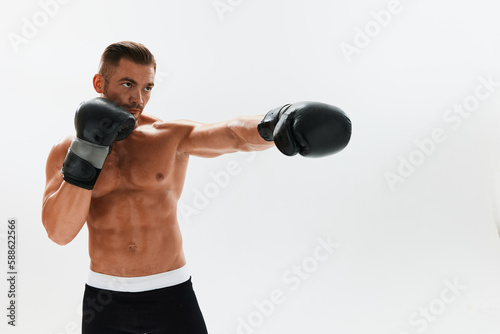 Man athletic bodybuilder poses in boxing gloves with nude torso abs in full-length background, boxing and martial arts. Advertising, sports, active lifestyle, light, competition, challenge concept.  © SHOTPRIME STUDIO