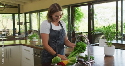 Happy caucasian pregnant woman wearing apron and washing vegetables in kitchen photo