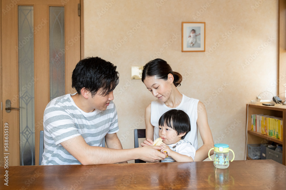 母親の膝の上に座り父親にバナナを食べさせてもらう子ども 母親の膝の上に座り父親にバナナを食べさせてもらう子ども