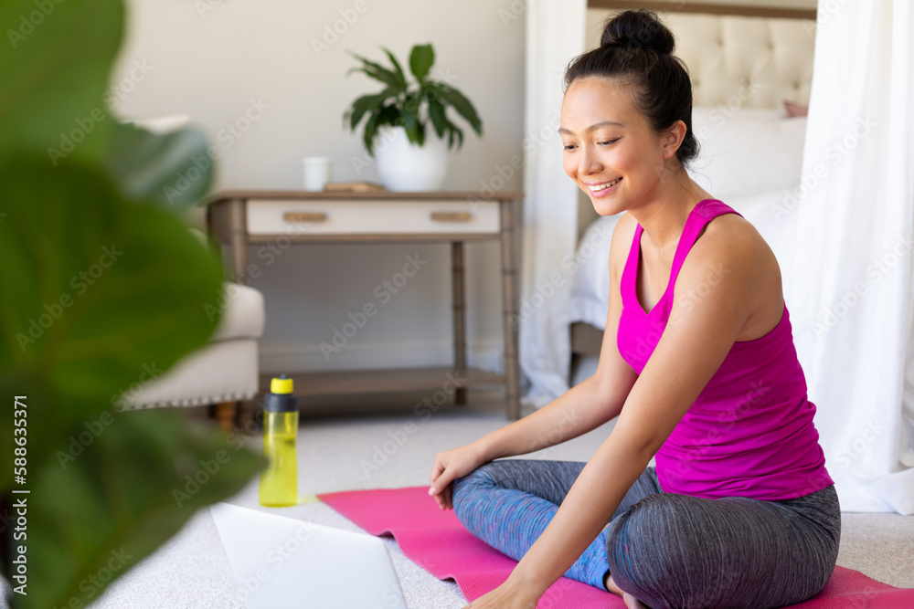 Happy asian woman doing yoga and using laptop in bedroom Happy asian woman doing yoga and using laptop in bedroom
