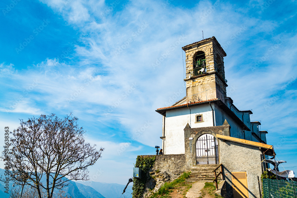 Naklejka premium The sanctuary at the top of the famous Monte Isola (Mount Island) in the middle of Lake Iseo, Italy. This is a typical hiking destination. Blue sky and white clouds on the background.