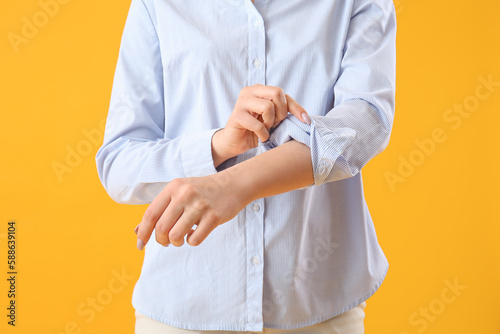 Young woman rolling up her sleeve on yellow background