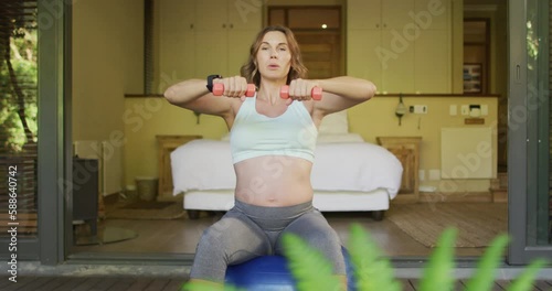 Caucasian pregnant woman exercising with weights and ball at home photo