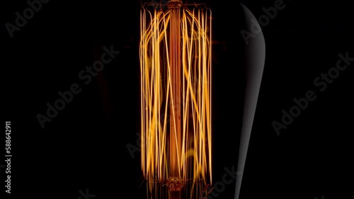 Close-up view of vintage Edison light bulb with orange filament spiral light on black background.