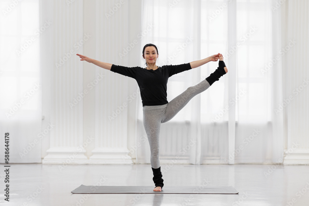 Cheerful young woman doing utthita hasta padagusthasana in the gym while yoga classes. Concept of flexibility, leg and back muscle tone, balance and concentration