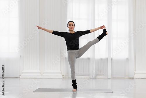 Fototapeta Naklejka Na Ścianę i Meble -  Cheerful young woman doing utthita hasta padagusthasana in the gym while yoga classes. Concept of flexibility, leg and back muscle tone, balance and concentration