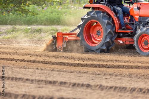Fotografie Tractor cultivating land with a rotary tiller in farm.