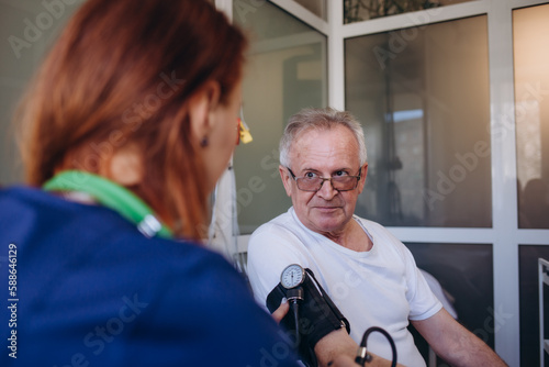 Female professional doctor examining elderly old male patient measuring high low arterial blood pressure using medical tonometer at hospital checkup appointment visit. Seniors hypertension concept