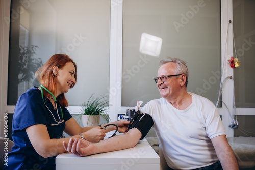 Female professional doctor examining elderly old male patient measuring high low arterial blood pressure using medical tonometer at hospital checkup appointment visit. Seniors hypertension concept