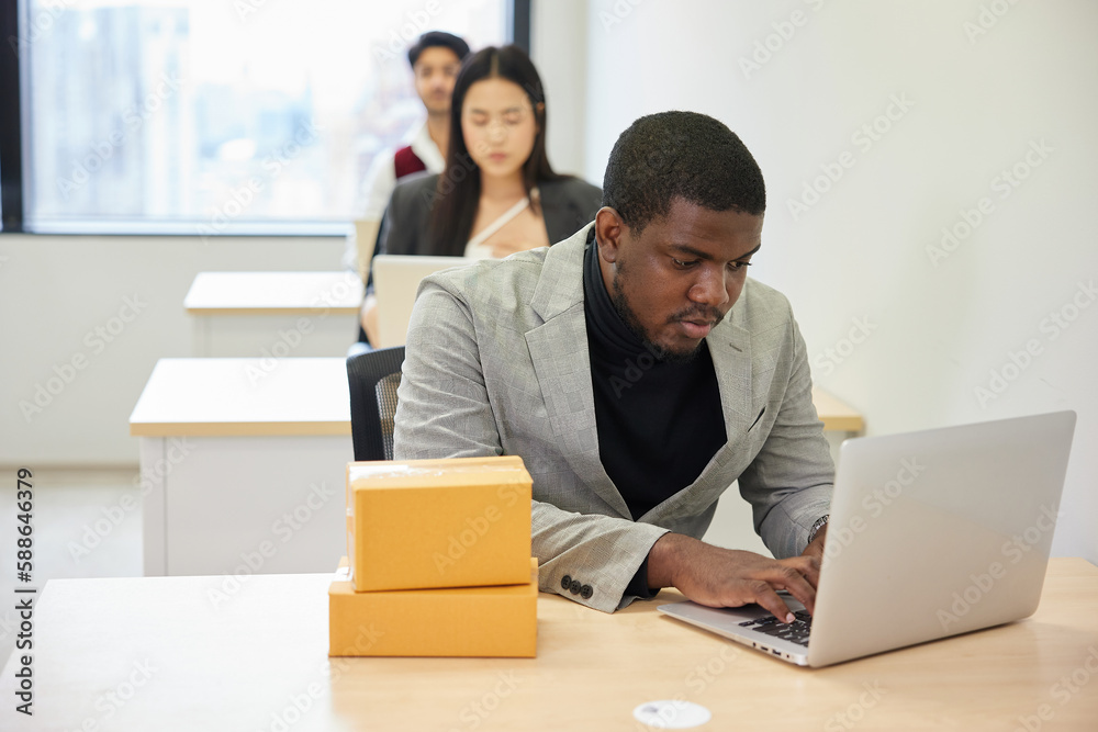 African businessman using laptop computer and checking parcel cardboard boxes from online shopping in the office African businessman using laptop computer and checking parcel cardboard boxes from online shopping in the office