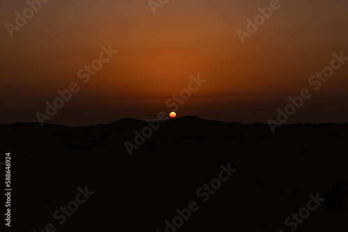 Sun setting above sand dunes in the desert