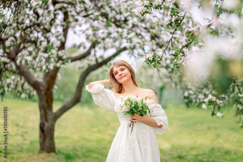 A beautiful young girl stands among the flowering trees. White flowers. Spring. A girl with her hair in a white dress. Portrait. Romance.
