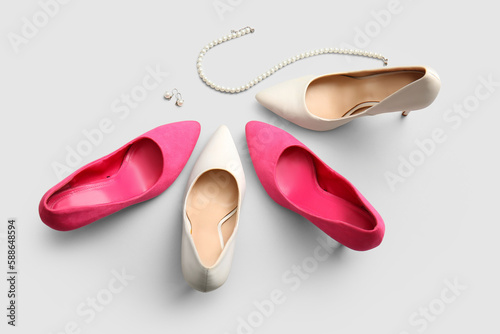 Stylish high heeled shoes and jewellery on light background