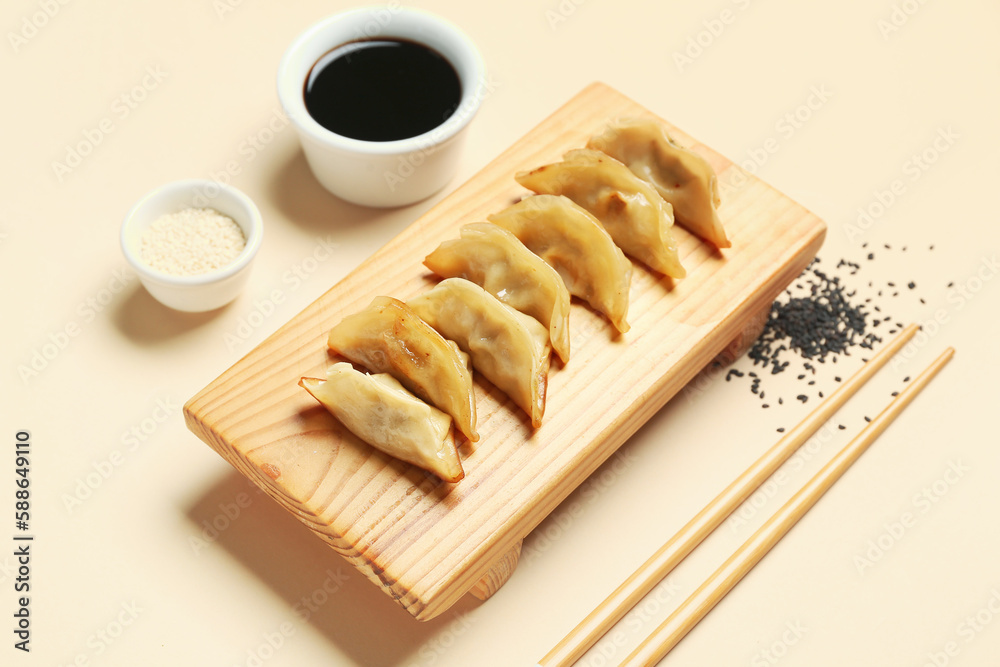 Wooden board with tasty Chinese jiaozi, sesame and sauce on beige background