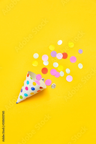 Composition with party hat and confetti on yellow background