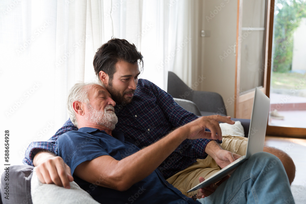 Senior mature father and adult son using laptop computer with happy and smiling together at home