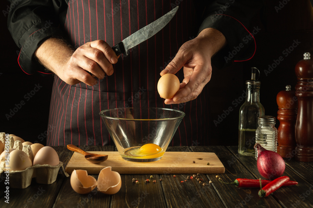 Cooking a delicious omelet for breakfast from eggs by the chef's hands. Work environment on the kitchen table. Egg in the cook hand Cooking a delicious omelet for breakfast from eggs by the chef's hands. Work environment on the kitchen table. Egg in the cook hand