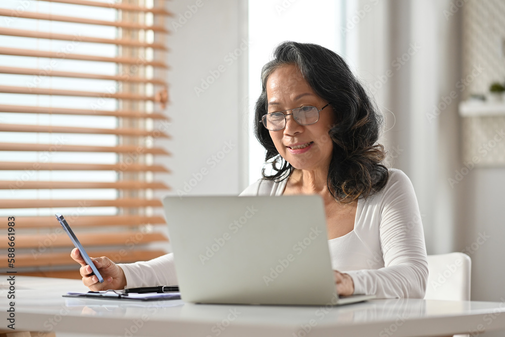 Positive middle aged woman watching training class, online webinar on laptop computer at comfortable home Positive middle aged woman watching training class, online webinar on laptop computer at comfortable home